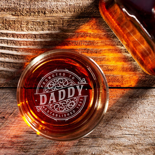 Personalized whiskey glass with 'Promoted to Daddy' engraving on rustic wood table