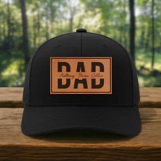 Personalized black dad hat with leather patch, custom names, outdoors on wood table