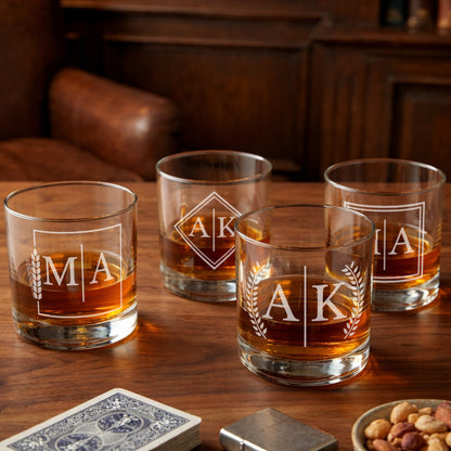 Set of four personalized whiskey glasses with etched initials on wooden table