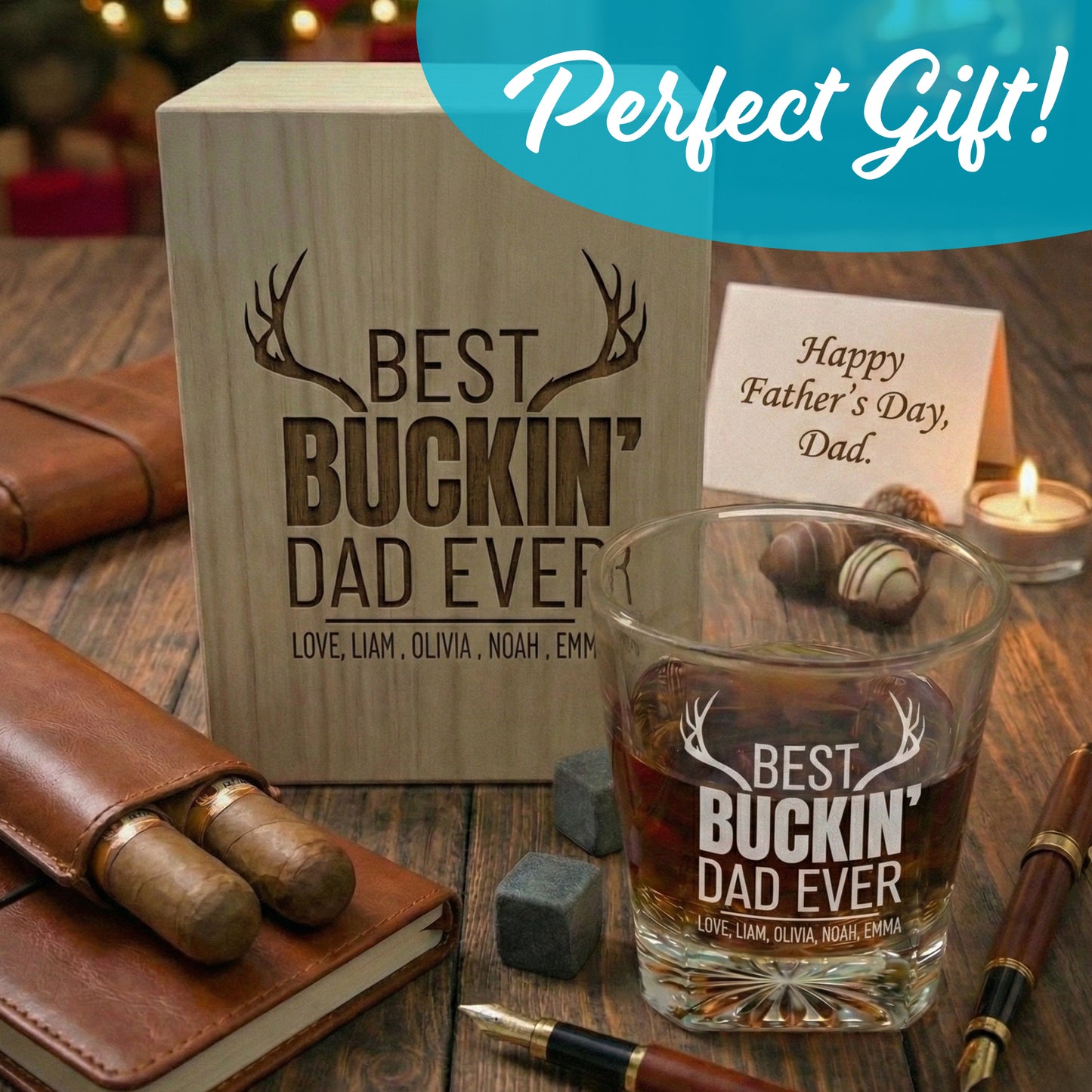 Personalized Father's Day whiskey glass and wooden box gift set with Best Buckin' Dad Ever engraving, cigars, chocolates, and a greeting card on a rustic table.